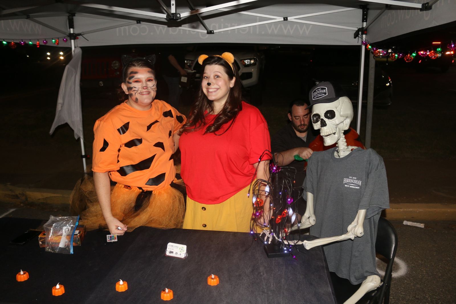 Costumed volunteers smiling at a decorated Halloween booth at a past Downtown Muskogee Halloween Boo-nanza